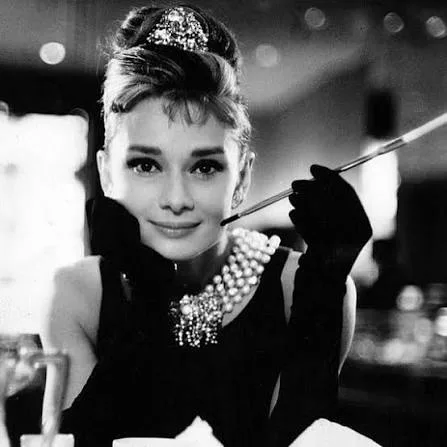 Audrey Hepburn in black with strands of pearl necklace smoking, for film Breakfast at Tiffany's(1961)
