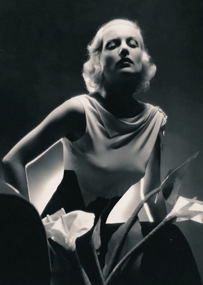 Carole Lombard in a black and white two tone sleeveless gown, with flowers in the foreground
