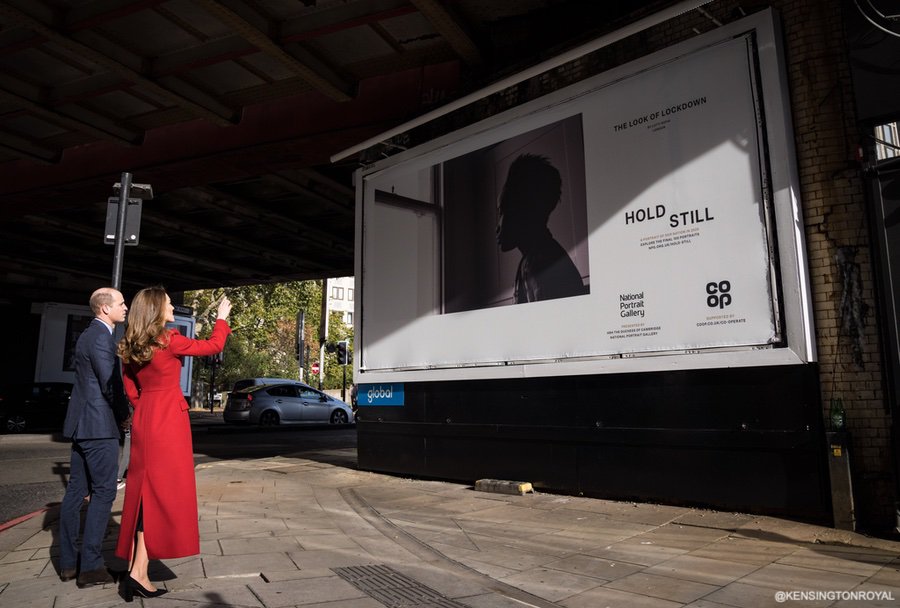 Kate Middleton Duchess of Cambridge custom made/bespoke Alexander McQueen red double breast full length coat with peak lapel for Hold Still photography project at Waterloo Station in London 