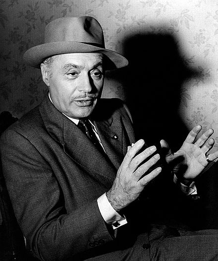 Charles Boyer in a dark suit and felt hat, 1955