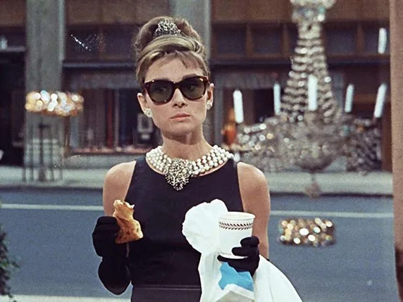 Audrey Hepburn in the black Givenchy dress with pearls and sunglasses, eating a pastry, Breakfast at Tiffany's (film, 1961)