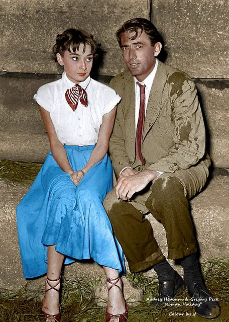 Colorized photo of Audrey Hepburn in a blue skirt sitting with Gregory Peck, Roman Holiday