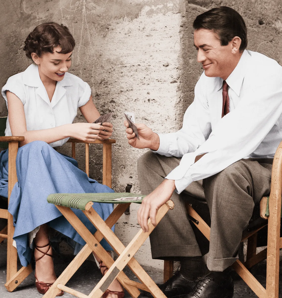 Colorized photo of Audrey Hepburn in a blue skirt with Gregory Peck in director's chairs, Roman Holiday