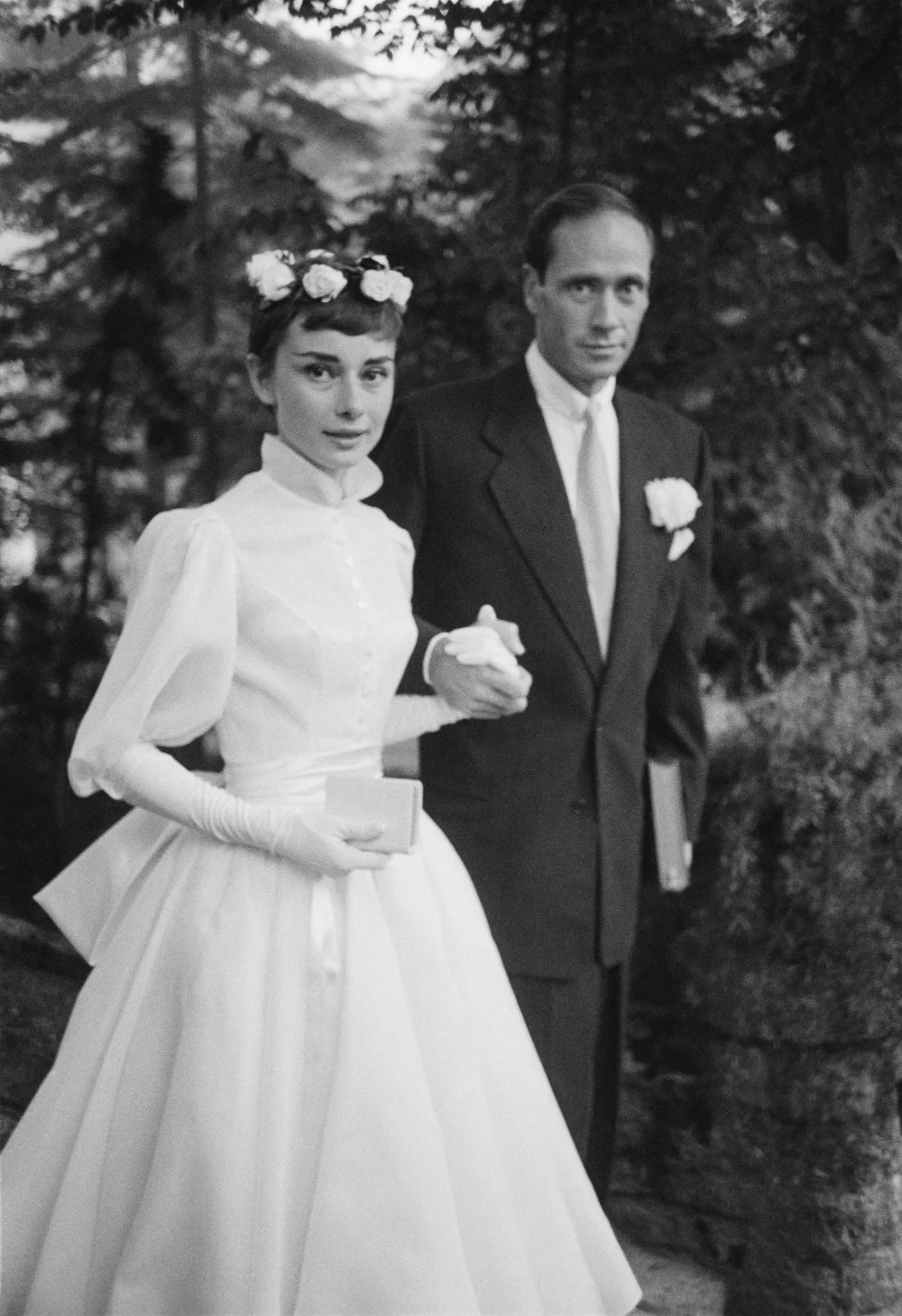 Audrey Hepburn in her white wedding dress and gloves, adjusting her flower crown, 1954