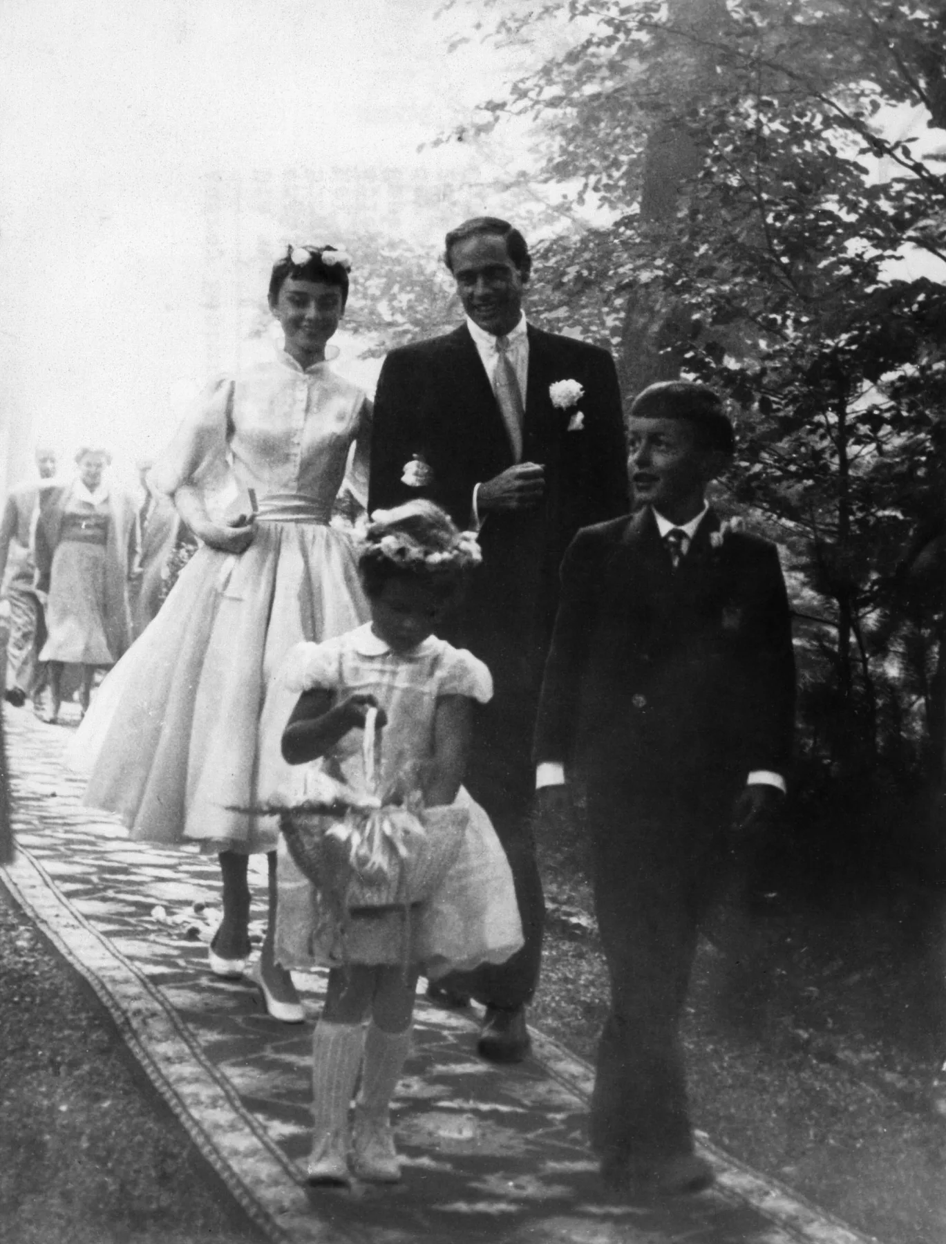 Audrey Hepburn and Mel Ferrer walking on their wedding day with a flower girl, Bürgenstock, 1954