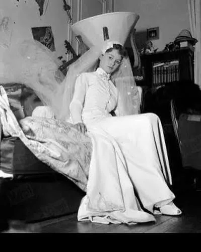 Brigitte Bardot seated in her wedding dress with a high collar, buttoned bodice and long veil, 1952