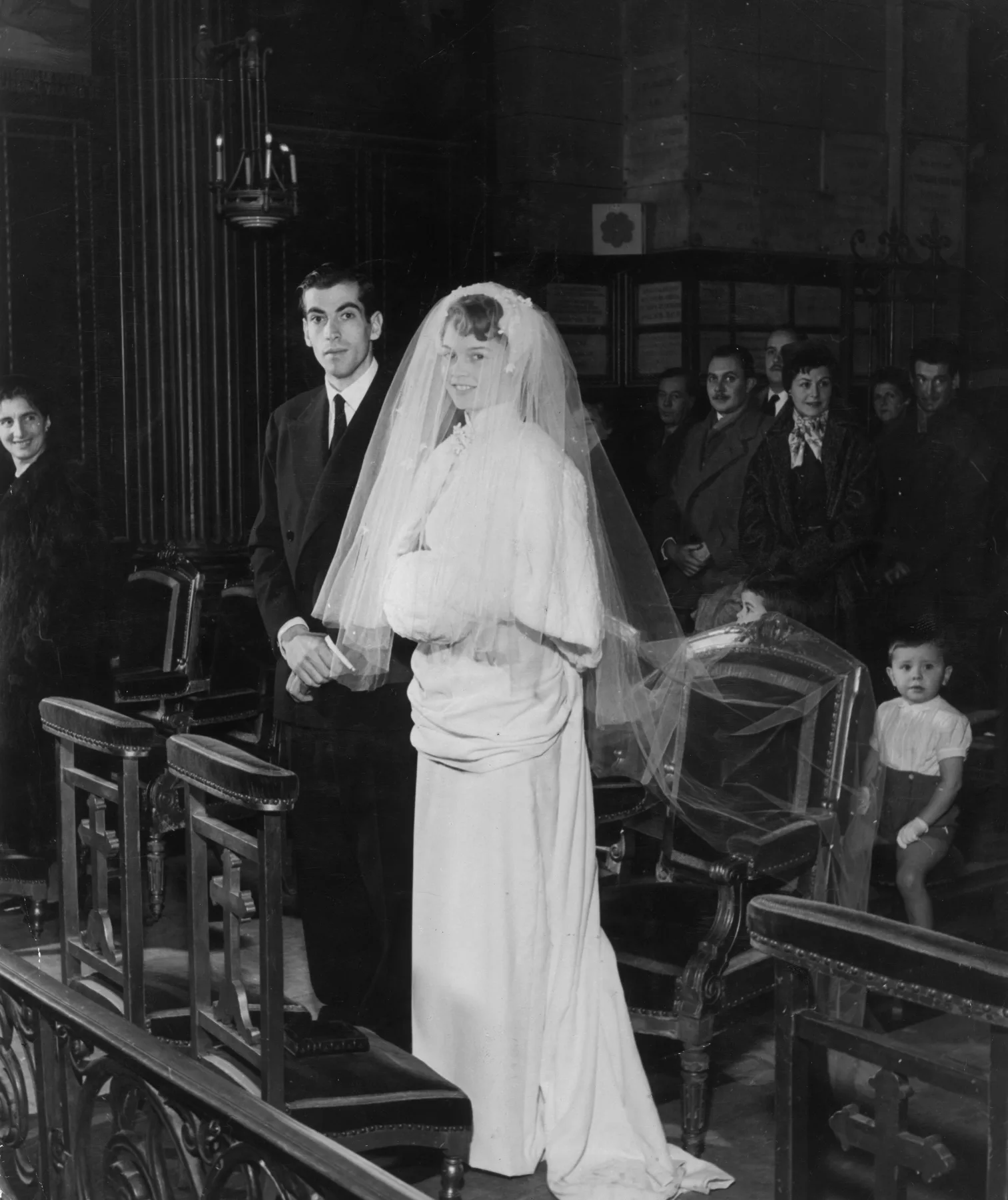 Brigitte Bardot in her wedding dress and veil standing beside Roger Vadim in church, 1952