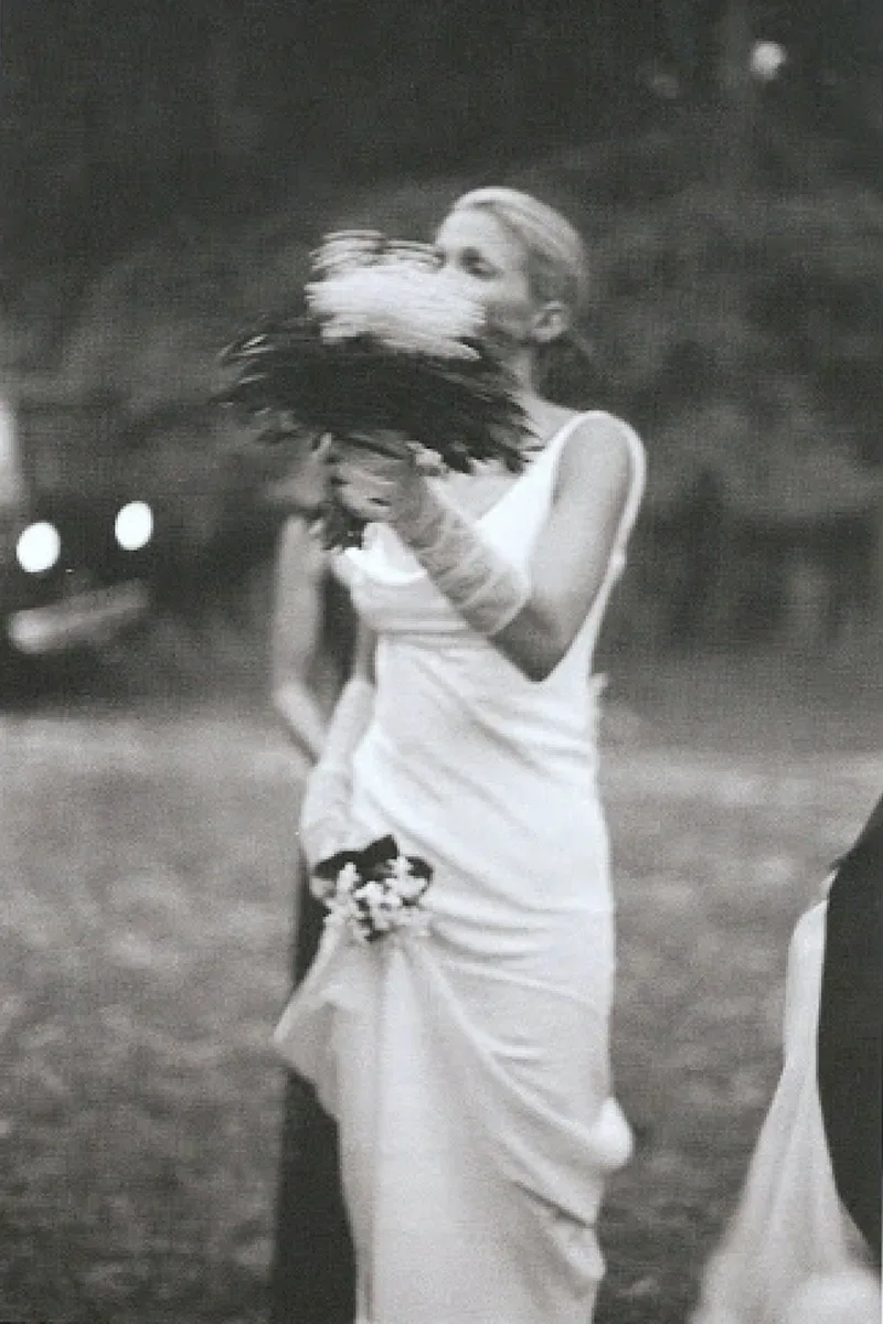 Carolyn Bessette in her bias-cut wedding dress, holding her bouquet to her face, 1996