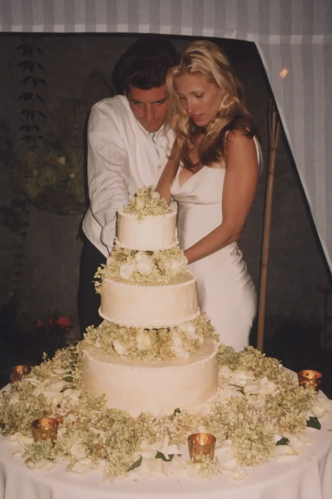 Carolyn Bessette in her slip dress and veil as John F. Kennedy Jr. kisses her hand, 1996
