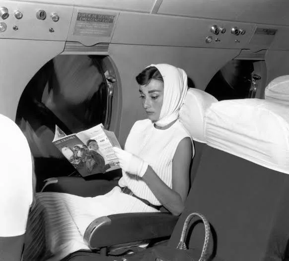 Audrey Hepburn in airplane reading wearing a headscarf