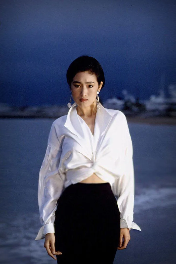 Gong Li in a white knotted shirt and black column skirt on the beach at Cannes, 1993