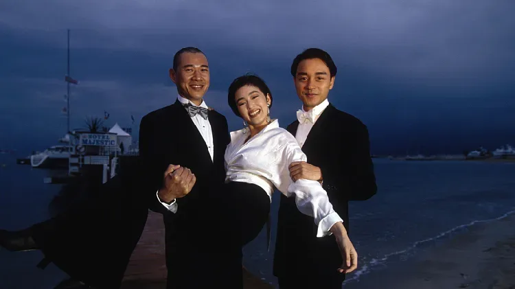 Gong Li in a white shirt held by Zhang Fengyi and Leslie Cheung by the sea at Cannes, 1993