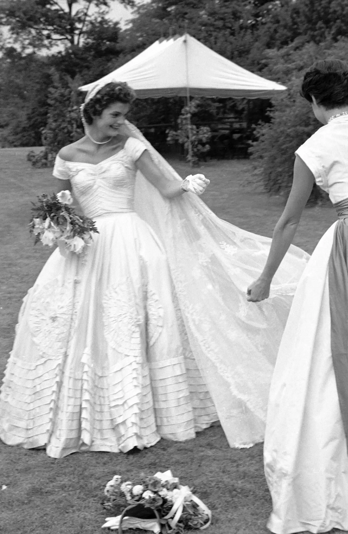 An attendant arranging the veil and train of Jacqueline Bouvier on the lawn, 1953