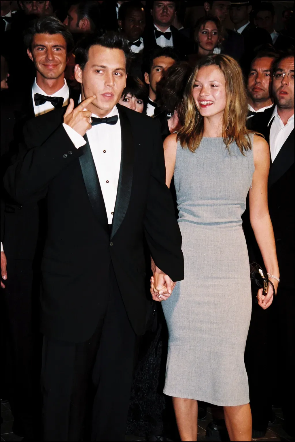 Kate Moss in her grey shift dress holding hands with Johnny Depp in a tuxedo among the crowd at Cannes, 10 May 1997