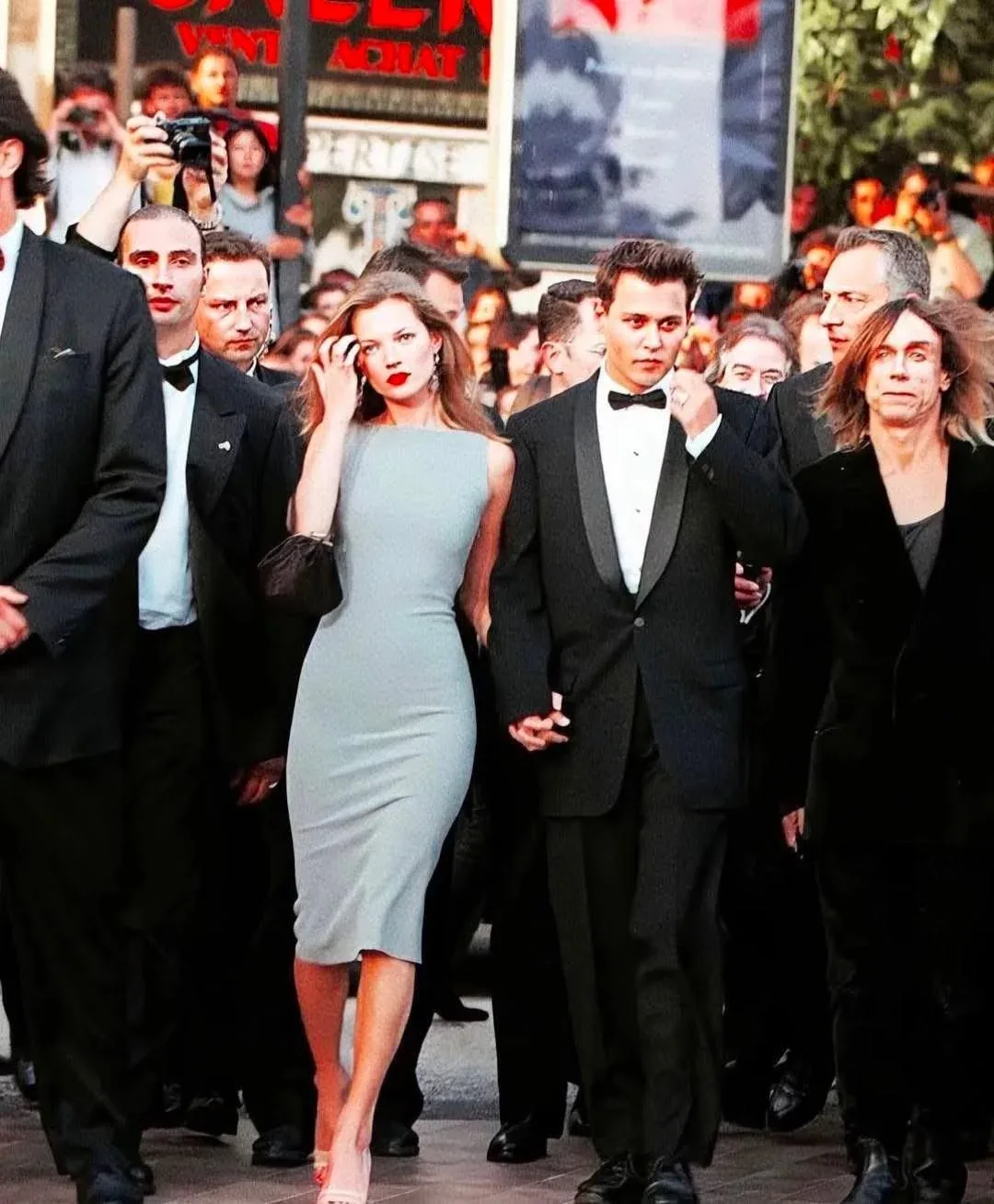 Kate Moss in her grey Narciso Rodriguez dress, carrying a small black handbag, walking with Johnny Depp through the crowd at Cannes, 1997