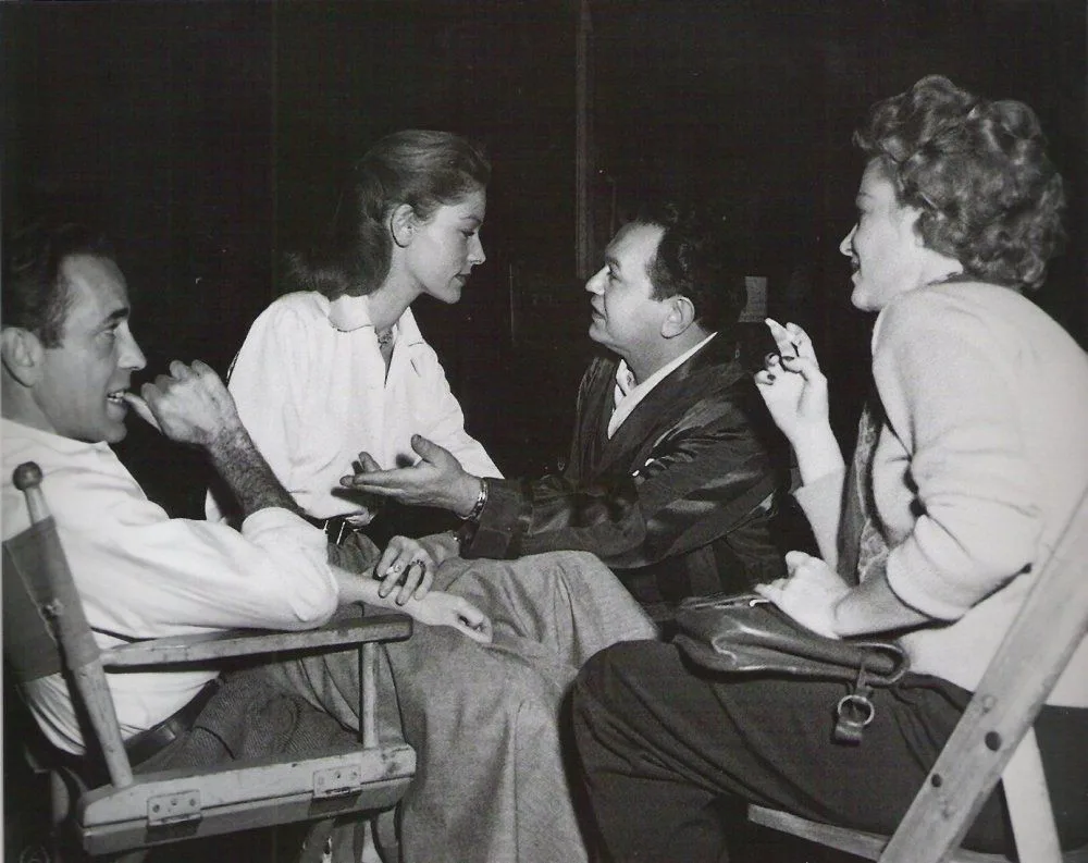 Lauren Bacall in her white shirt with cast and crew on the set of Key Largo, 1948