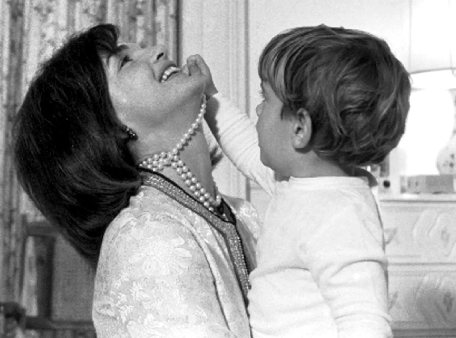 John F. Kennedy Jr. with his mother Jackie Kennedy, playing her pearl necklace, 1960s.