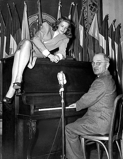 Lauren Bacall sitting on a piano played by Vice President Harry S. Truman at the National Press Club, Washington, 10 February 1945